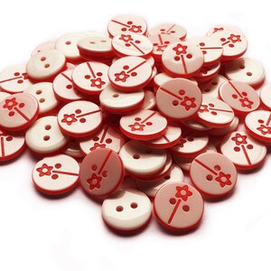 May include: A pile of white buttons with a red flower design. The buttons are round and have two holes.