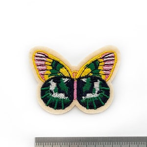May include: An embroidered butterfly patch in green, yellow and pink, with a ruler for scale. The butterfly is approximately 3 cm wide.