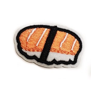 以下が含まれることがあります： サーモンの寿司ロールの刺繍アイロン接着パッチのクローズアップ。パッチは白で、黒いアウトラインとオレンジのサーモンフィリングです。