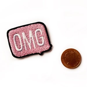May include: Pink embroidered iron-on patch with a black border and white text that says "OMG".