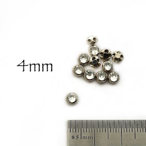 May include: A collection of small, clear rhinestones with a silver-colored metal base. The text "4mm" is next to the rhinestones. A metal ruler is in the foreground, showing millimeter measurements.