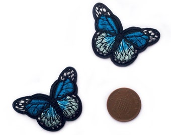 Op de afbeelding: Twee geborduurde blauwe en witte vlinder strijkpatches. De patches zijn ongeveer zo groot als een Nederlandse cent.