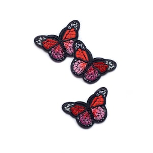 May include: Three embroidered butterfly patches in shades of red and pink with black outlines.