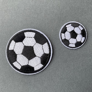 Op de afbeelding: Twee geborduurde voetbalpatches. Een grote en een kleine. De voetballen zijn zwart en wit met een witte rand. De patches zijn rond en liggen op een grijze ondergrond.