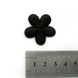 Peut inclure: Un patch brodé de fleur noire, d'environ 2 cm de diamètre, avec cinq pétales. Le patch est présenté à côté d'une règle pour référence de taille.