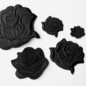 Könnte beinhalten: Eine Sammlung schwarzer Rosenaufnäher in verschiedenen Größen. Die Aufnäher sind mit detaillierten Rosendesigns bestickt, die Blütenblätter und Blätter zeigen. Die Aufnäher sind auf weißem Hintergrund angeordnet, was die feinen Details der floralen Stickerei hervorhebt.