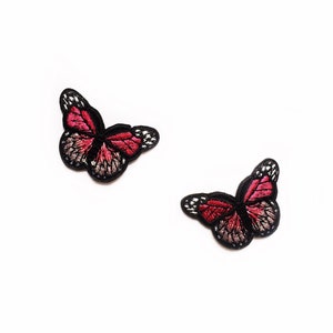 May include: Two embroidered iron-on patches featuring pink butterflies with black outlines.