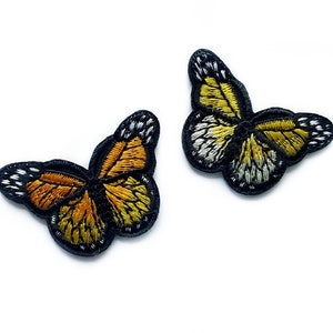 May include: Two embroidered butterfly patches, one yellow and one orange, with black outlines and white accents. The patches are ideal for adding a touch of whimsy to clothing, bags, or other crafts.