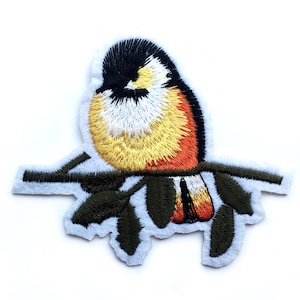 Puede incluir: Parche bordado para planchar de un pájaro amarillo y naranja posado en una rama verde.