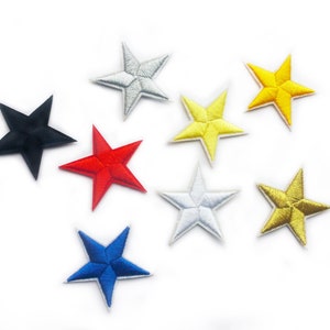 Pode incluir: Uma coleção de patches de estrelas bordadas em várias cores, incluindo preto, vermelho, azul, amarelo, prata e dourado. Estes patches são provavelmente para fins decorativos, como embelezar roupas ou acessórios. As estrelas estão dispostas sobre um fundo branco.
