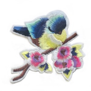 May include: Embroidered iron-on patch featuring a blue and yellow bird perched on a branch with pink and purple flowers.