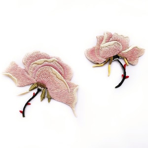 May include: Two pink embroidered rose flower patches with gold and black stems. The roses have a light pink and white color gradient.