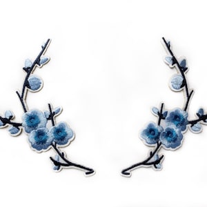 May include: Two blue embroidered flower patches with a white background. Each patch features a delicate branch with blue flowers and leaves.
