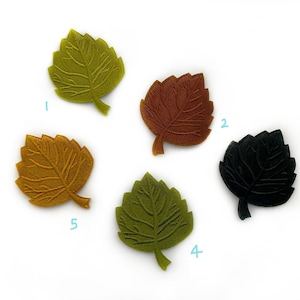 Può includere: Cinque forme di foglie in feltro di diversi colori: verde, giallo, arancione, marrone e nero. Le foglie sono tutte della stessa dimensione e forma, e sono disposte in cerchio su uno sfondo bianco.