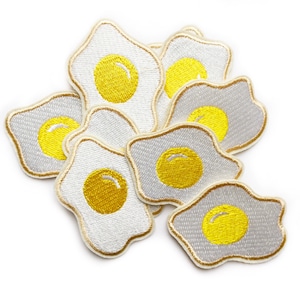 May include: A set of eight white felt iron-on patches shaped like fried eggs with yellow embroidered yolks.