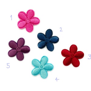 Può includere: Cinque toppe ricamate a forma di fiore in vari colori: rosa, blu navy, rosso, turchese e viola. Ogni fiore ha cinque petali e un centro circolare. Le toppe sono su sfondo bianco.