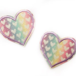 May include: Two rainbow-coloured heart-shaped patches with a white background and a purple outline. The hearts are covered in a pattern of smaller white hearts.
