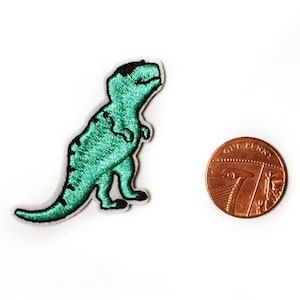 May include: A green embroidered dinosaur patch with black stitching. The patch is about the size of a British one penny coin.
