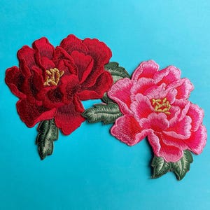 May include: Two embroidered fabric flower patches, one red and one pink, with green leaves. The flowers are in a peony style.