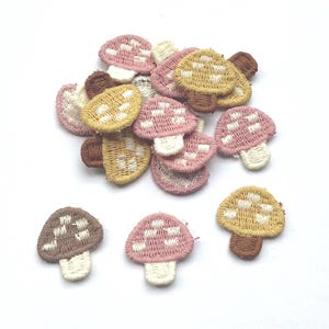 Op de afbeelding: Een verzameling geborduurde paddenstoelpatches in verschillende kleuren, waaronder roze, geel en bruin. Elke patch heeft een wit geblokt patroon op de paddenstoelenkap en een witte steel. Deze patches zijn ideaal om een ​​vrolijke touch toe te voegen aan kleding of accessoires.