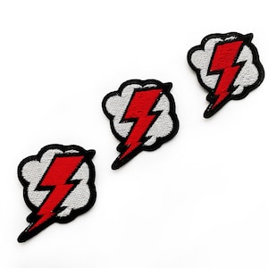 May include: Three embroidered patches featuring a red lightning bolt design centred on a white cloud shape with a thick black border. Each patch displays a jagged, vibrant red bolt of lightning layered over a textured white cloud background.