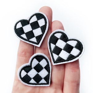 Peut inclure: Trois patchs en forme de cœur à carreaux noirs et blancs. Les patchs sont en tissu et ont un contour blanc.
