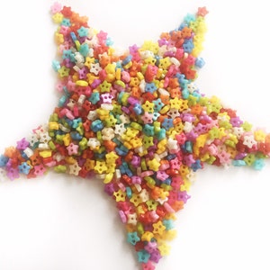 Può includere: Una forma a stella composta da numerose piccole perline a forma di stella in vari colori. Le perline includono rosso, giallo, blu, verde e rosa, creando un design luminoso e allegro. Lo sfondo è bianco.