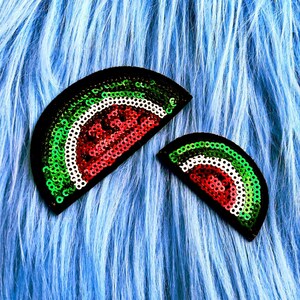 May include: Two semicircular patches shaped like watermelon slices, crafted with red, white, and green sequins. The larger patch is positioned to the left, while the smaller patch is to the right, both featuring a black border outline.