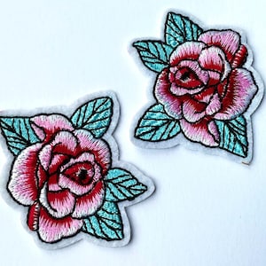 May include: Two embroidered iron-on patches featuring pink and red roses with teal green leaves.