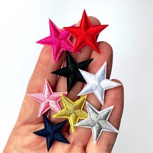 以下が含まれることがあります： ピンク、赤、黒、白、黄色、ネイビーブルー、シルバーなど、さまざまな色の刺繍された星のパッチのコレクション。これらの星型のパッチは、衣類やアクセサリーの装飾など、装飾目的で使用される可能性があります。