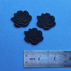 Op de afbeelding: Drie zwarte geborduurde rozenpatches op een blauwe achtergrond. De patches hebben gedetailleerde getextureerde stiksels, met een liniaal eronder voor de schaal. Elke roos meet ongeveer 3,8 cm in diameter.