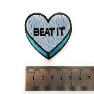 May include: A light blue heart-shaped patch with a blue outline and the text "BEAT IT" in black embroidery.