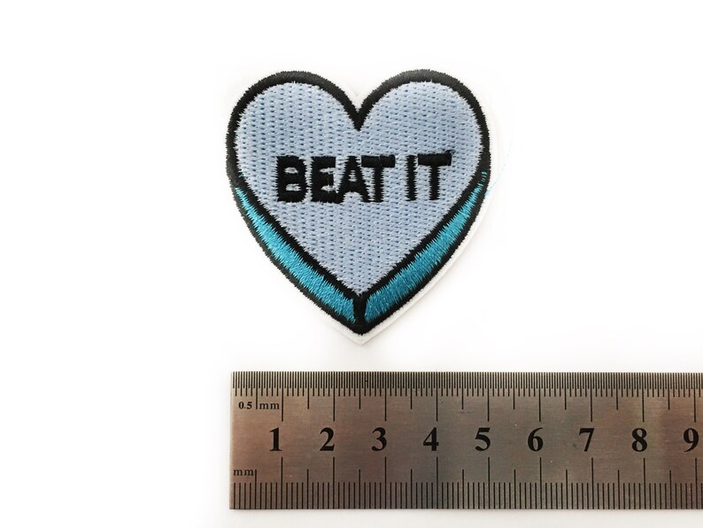 May include: A light blue heart-shaped patch with a blue outline and the text "BEAT IT" in black embroidery.