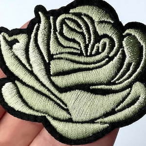 Op de afbeelding: Een groene geborduurde rozenpatch met zwarte stiksels. De roos is een enkele bloei met een gedetailleerd, gelaagd ontwerp.