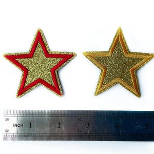 May include: Two gold glitter star-shaped iron-on patches, one with a red outline and the other with a gold outline. The patches are approximately 2 inches in size.