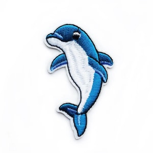 May include: An embroidered dolphin patch in blue and white. The dolphin is facing right and has a white belly and a blue back. The patch is ideal for adding a touch of whimsy to clothing, bags, or other accessories.