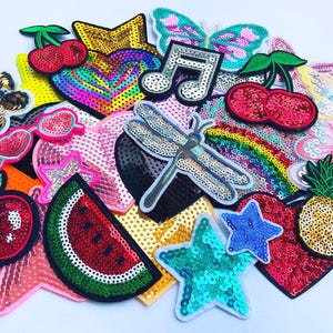 Op de afbeelding: Een verzameling kleurrijke pailletten patches in diverse vormen, waaronder sterren, harten, vlinders en fruit. De patches hebben levendige kleuren zoals rood, groen, goud en blauw, ideaal voor het opfleuren van kleding of accessoires.