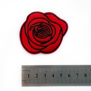 May include: Embroidered red rose patch with black detailing. The patch is approximately 5 cm in diameter. The rose is a classic floral design, suitable for clothing or accessories.
