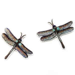 May include: Two embroidered dragonfly patches with iridescent blue and brown wings. The dragonflies are on a white background.