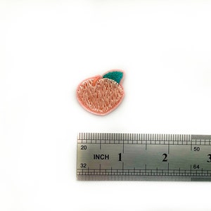 Puede incluir: Un parche bordado de melocotón rosa con una hoja verde, que mide aproximadamente 2,5 cm de diámetro.