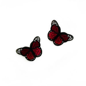 Può includere: Due toppe ricamate a forma di farfalla rossa con contorni neri e dettagli bianchi.