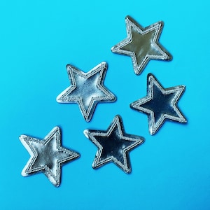 Pode incluir: Cinco patches de tecido em forma de estrela prateados sobre um fundo azul brilhante.