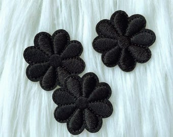 May include: Three black felt flower appliques with a daisy-like design. The appliques are on a white fuzzy background.