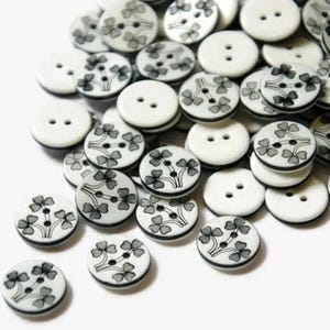 Könnte beinhalten: Ein Haufen weißer Knöpfe mit schwarzen Kleeblatt-Designs. Einige Knöpfe sind schlicht weiß.