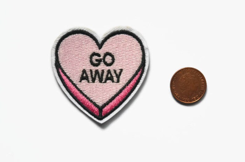 May include: Pink heart-shaped embroidered patch with the text "GO AWAY" in black lettering.