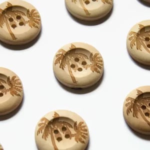 Puede incluir: Un conjunto de diez botones de madera con un diseño de palmera. Los botones son beige con palmeras marrones y tienen cuatro agujeros cada uno.