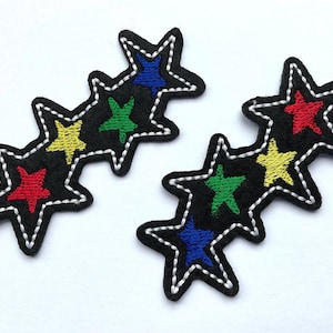 May include: Two black star patches with white stitched edges. Each patch features three stars in red, yellow, green, and blue. These embroidered patches are ideal for adding flair to clothing or accessories.