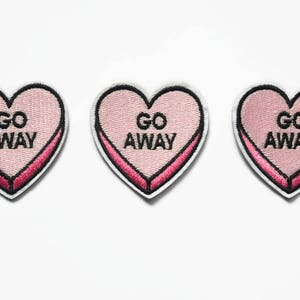 May include: Three pink heart-shaped patches with black outlines and the text "GO AWAY" in black.