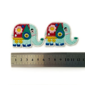 Op de afbeelding: Twee geborduurde strijkpatches van blauwe, groene, rode, gele en witte olifanten met bloemmotieven. De patches zijn ongeveer 5 cm lang.