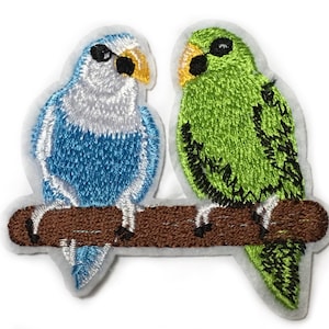 May include: Two embroidered birds perched on a brown branch. The bird on the left is blue and white, while the bird on the right is green.